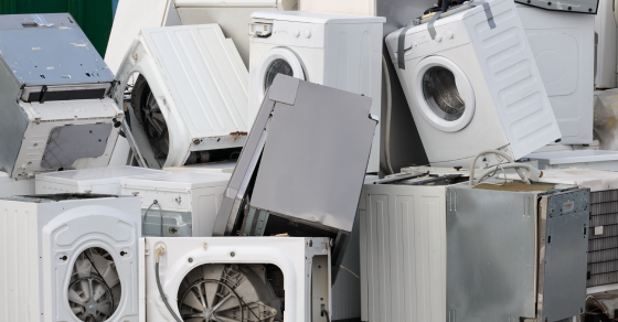 Pile of discarded washing machines stacked together outdoors.